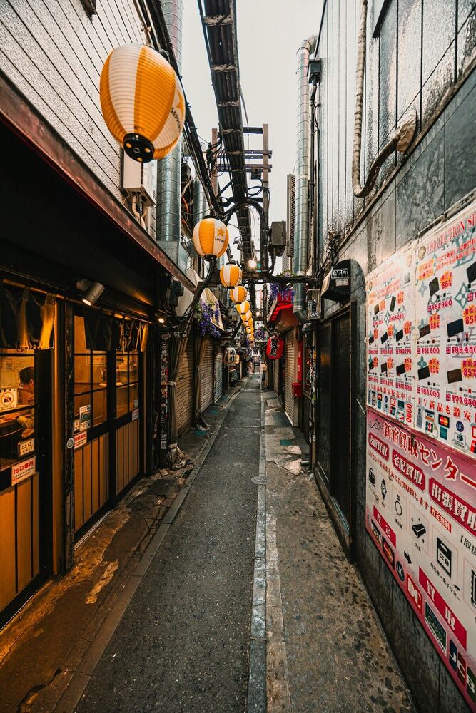 東京の横丁。提灯が並ぶ狭い路地に飲食店が軒を連ねる夕暮れの風景
