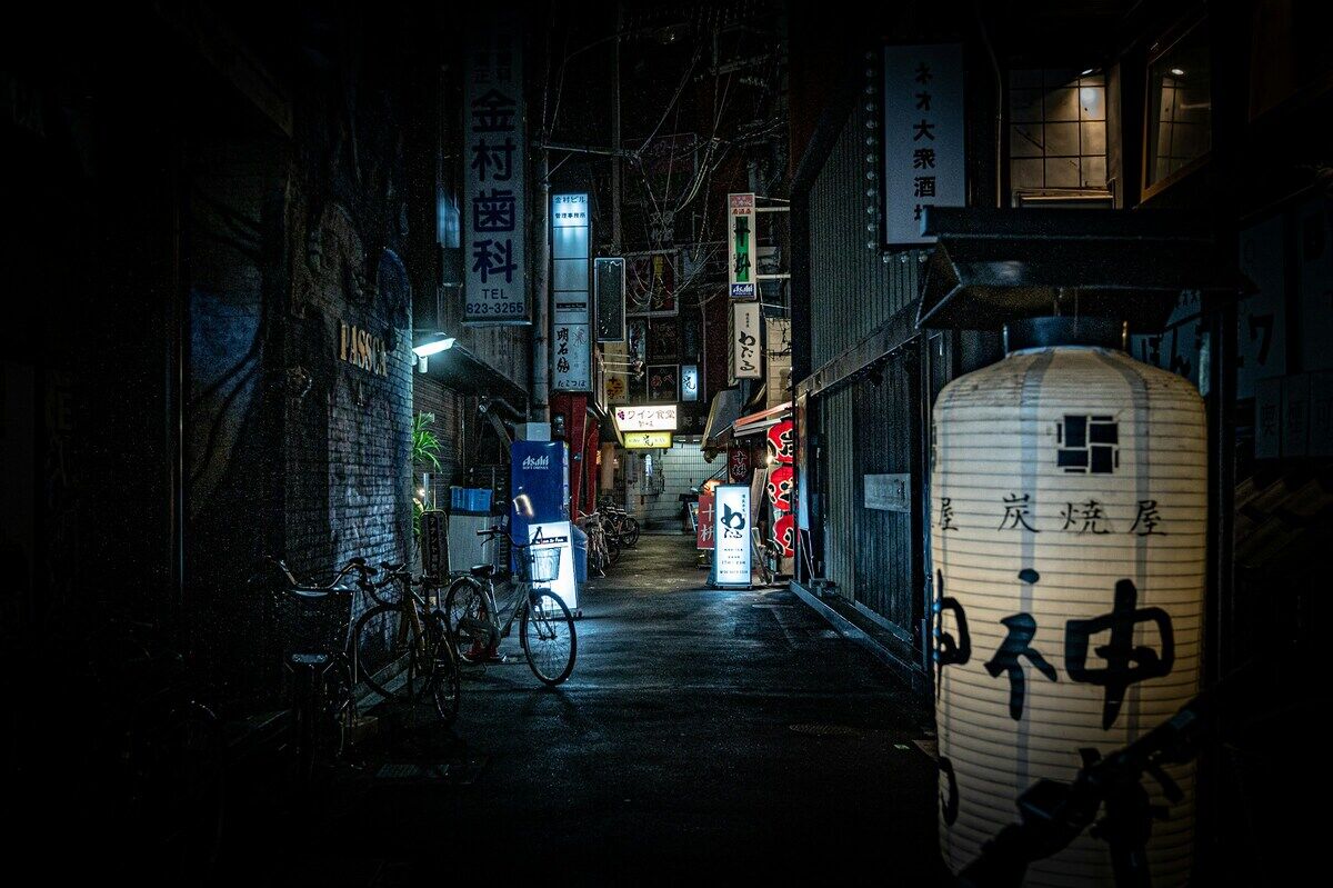 夜の路地。居酒屋の提灯が光る狭い通り