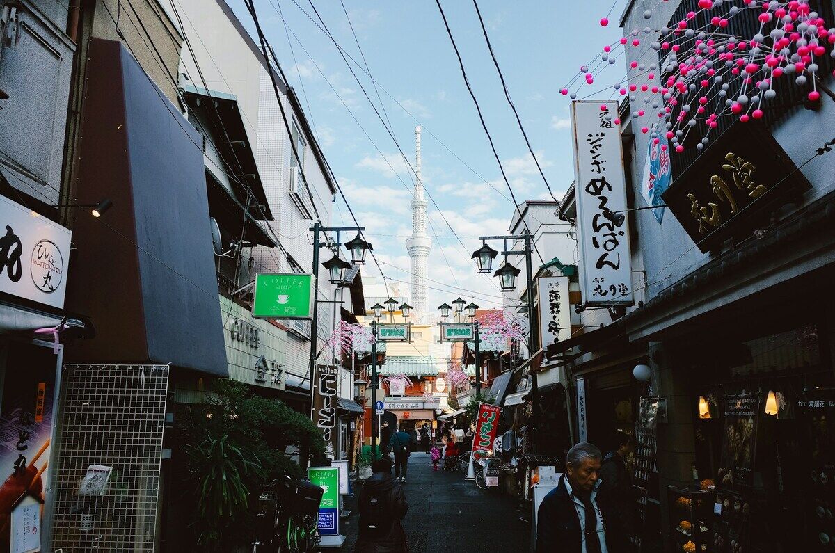 東京下町の商店街。看板が並ぶ通りの奥に東京スカイツリーが見える